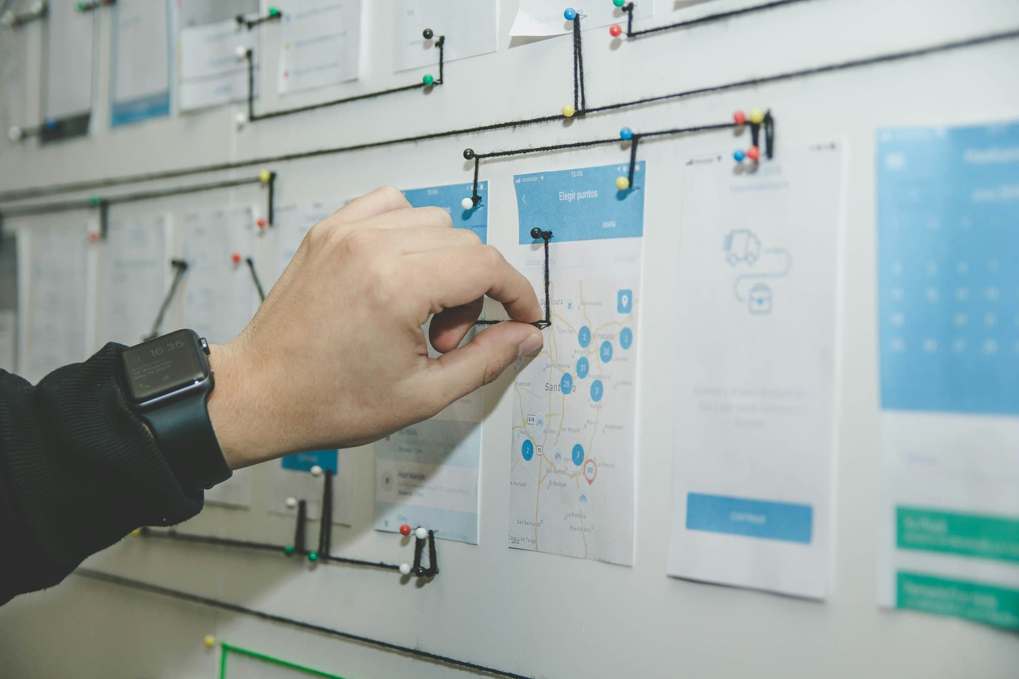 Hand die een schets vastprikt op een planningsbord met wireframes